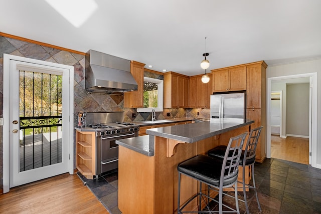 kitchen with sink, wall chimney exhaust hood, dark hardwood / wood-style flooring, a kitchen island, and appliances with stainless steel finishes