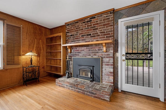 living room featuring built in shelves, crown molding, hardwood / wood-style floors, and a brick fireplace