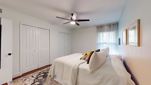 bedroom featuring multiple closets, hardwood / wood-style floors, and ceiling fan