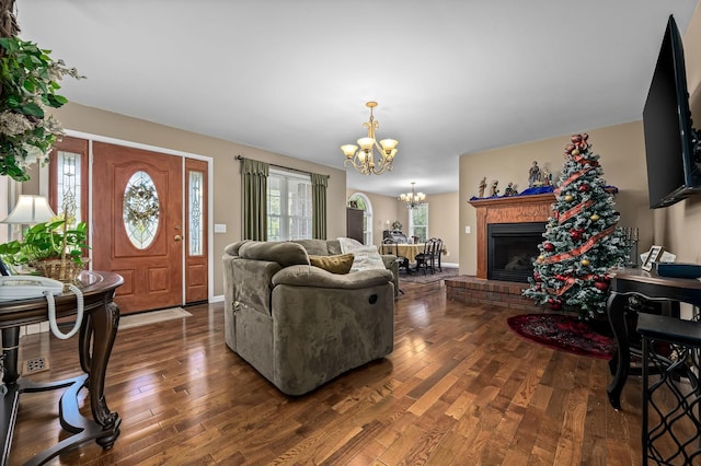 living room with a brick fireplace, dark wood-type flooring, and an inviting chandelier