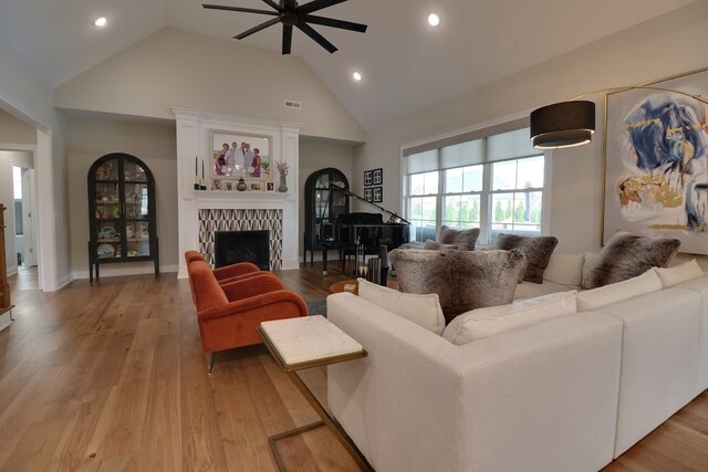 living room featuring a tiled fireplace, ceiling fan, high vaulted ceiling, and light hardwood / wood-style floors