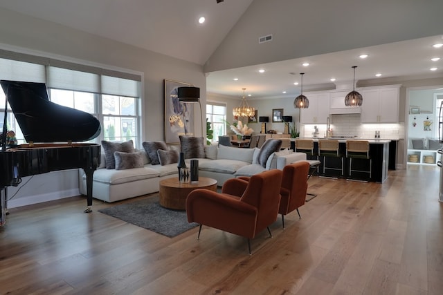 living room with an inviting chandelier, high vaulted ceiling, sink, and light hardwood / wood-style floors