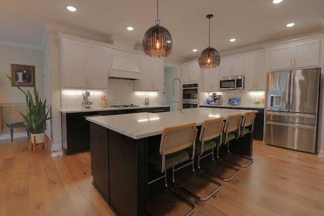 kitchen with appliances with stainless steel finishes, hanging light fixtures, custom range hood, white cabinets, and a kitchen island