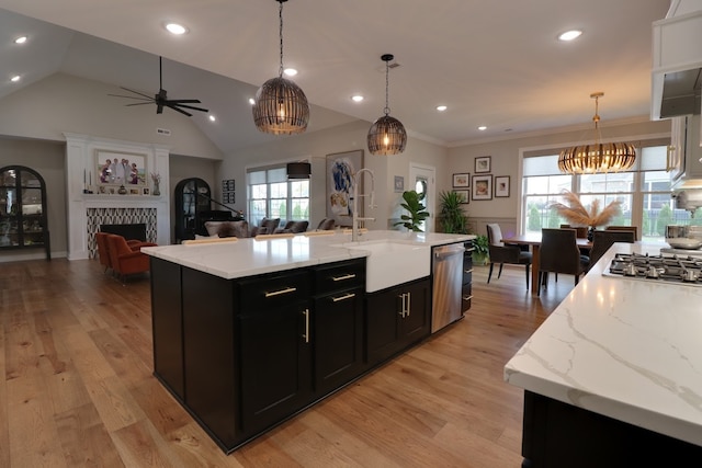 kitchen with sink, hanging light fixtures, appliances with stainless steel finishes, a tiled fireplace, and a kitchen island with sink