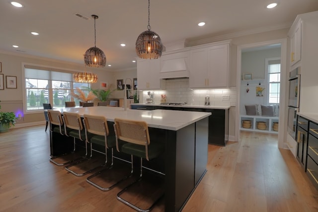 kitchen featuring plenty of natural light, a kitchen island with sink, hanging light fixtures, and white cabinets