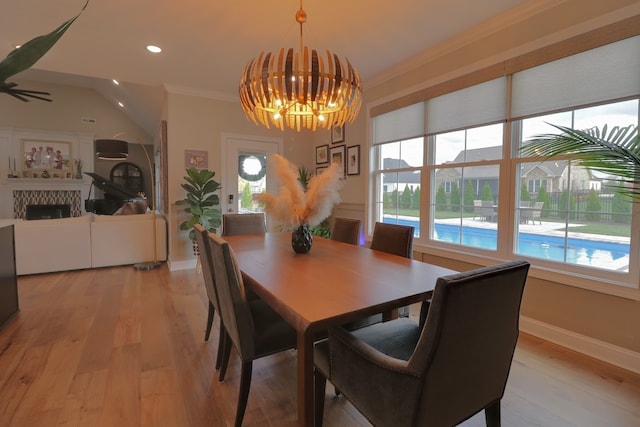 dining area featuring a tile fireplace, light wood-type flooring, a chandelier, and crown molding