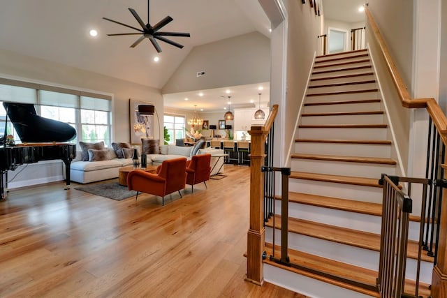 living room with high vaulted ceiling, ceiling fan with notable chandelier, and light hardwood / wood-style floors