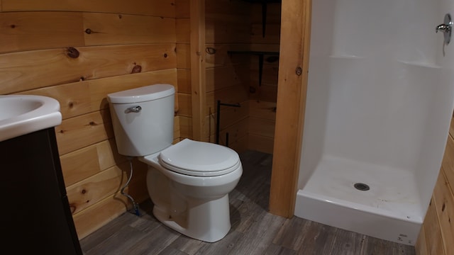 bathroom featuring vanity, a shower, wooden walls, hardwood / wood-style flooring, and toilet