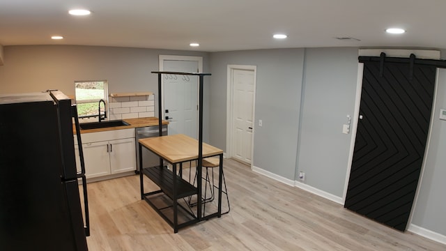 kitchen featuring black fridge, stainless steel dishwasher, sink, a barn door, and white cabinets