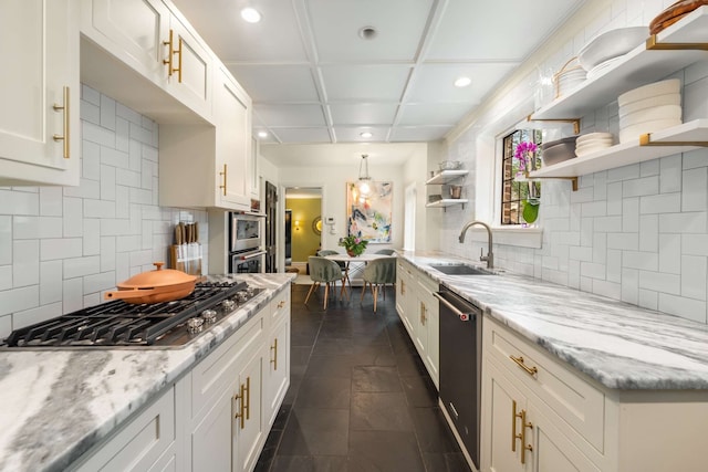 kitchen with backsplash, light stone counters, stainless steel appliances, sink, and white cabinetry