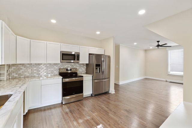 kitchen featuring white cabinets, light hardwood / wood-style flooring, ceiling fan, tasteful backsplash, and stainless steel appliances