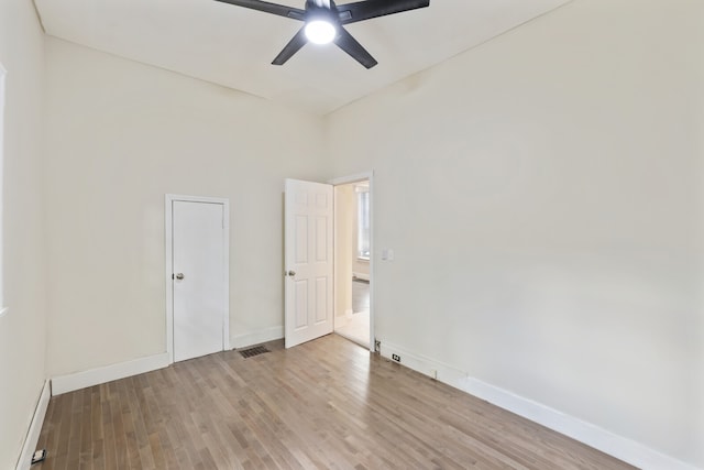 empty room featuring ceiling fan, light wood-type flooring, and a high ceiling