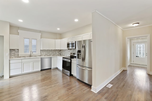 kitchen with white cabinets, crown molding, sink, light hardwood / wood-style floors, and stainless steel appliances