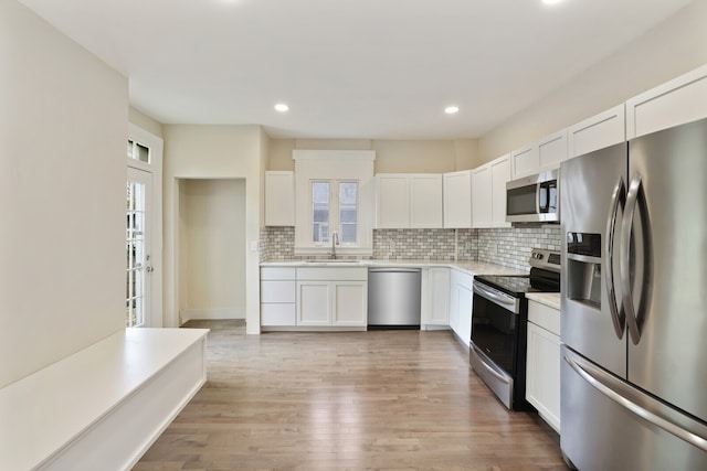 kitchen with decorative backsplash, appliances with stainless steel finishes, light hardwood / wood-style flooring, and white cabinetry