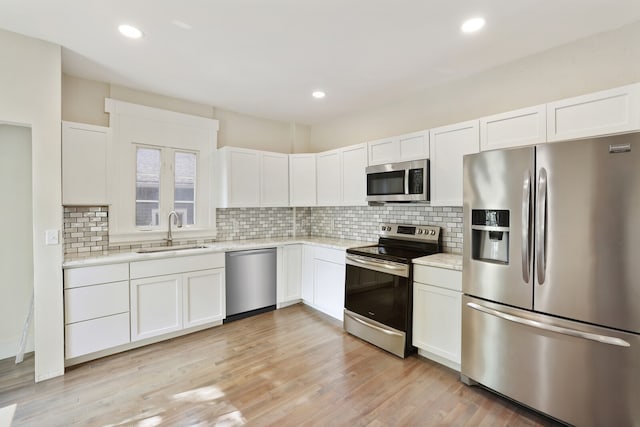 kitchen featuring sink, stainless steel appliances, decorative backsplash, white cabinets, and light wood-type flooring