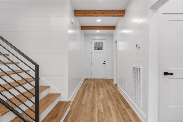 hallway featuring wood walls, beam ceiling, and light wood-type flooring