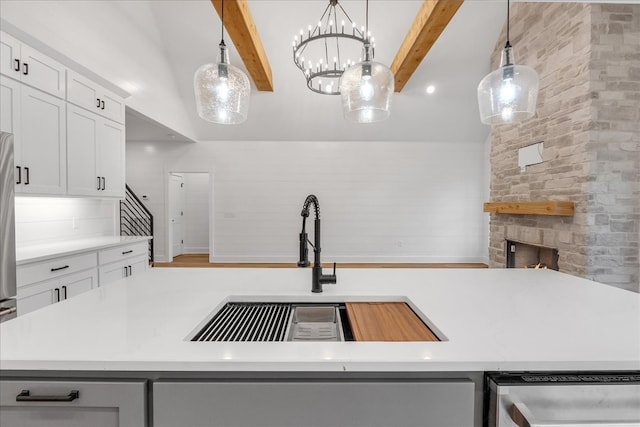 kitchen featuring white cabinets, a fireplace, beam ceiling, and hanging light fixtures