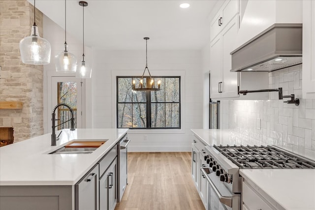 kitchen featuring pendant lighting, custom exhaust hood, sink, decorative backsplash, and appliances with stainless steel finishes