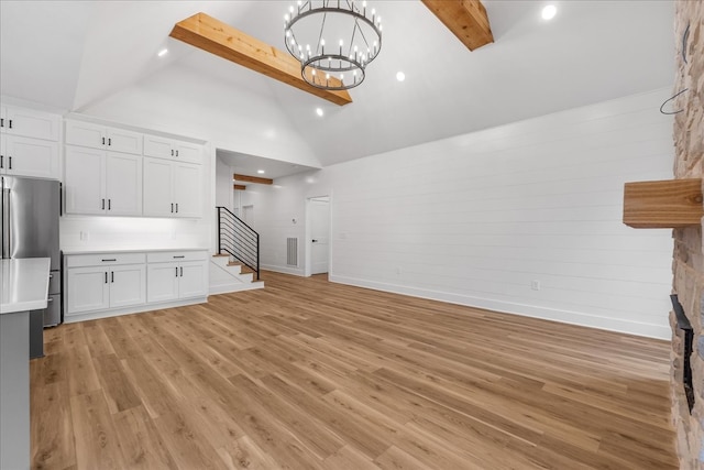 unfurnished living room featuring an inviting chandelier, beamed ceiling, high vaulted ceiling, a fireplace, and light wood-type flooring