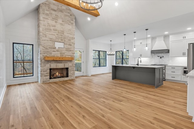 kitchen featuring light wood-type flooring, custom exhaust hood, high vaulted ceiling, white cabinets, and an island with sink