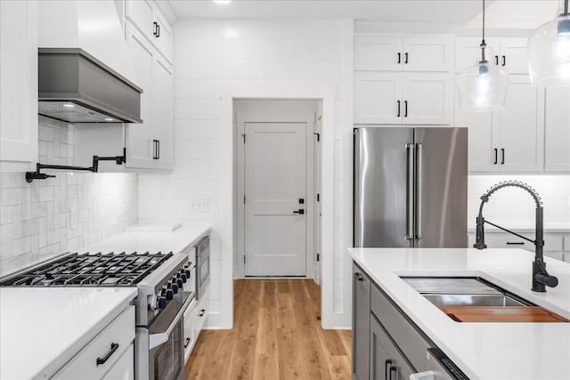 kitchen with premium appliances, sink, decorative light fixtures, white cabinets, and light hardwood / wood-style floors