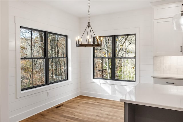 unfurnished dining area featuring wooden walls, a healthy amount of sunlight, a notable chandelier, and light wood-type flooring