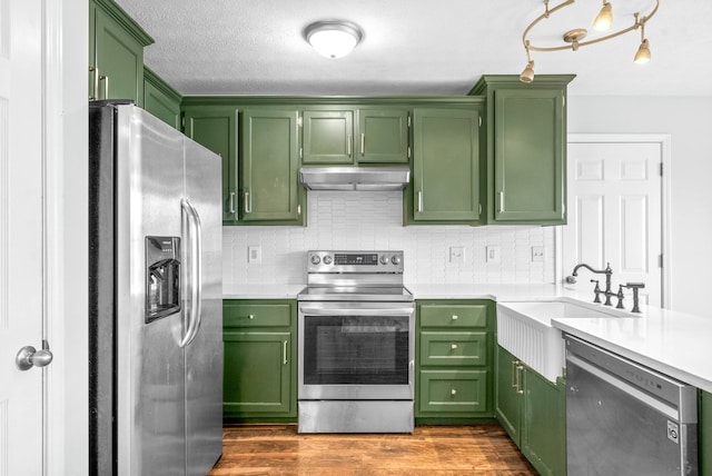 kitchen featuring hardwood / wood-style floors, backsplash, green cabinets, sink, and stainless steel appliances