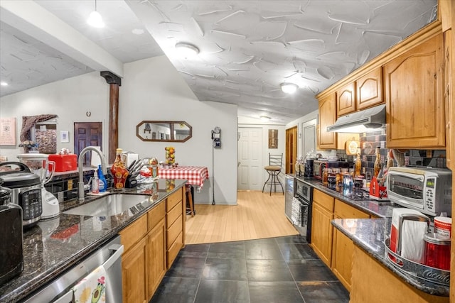 kitchen with sink, dark stone counters, vaulted ceiling, black appliances, and light wood-type flooring