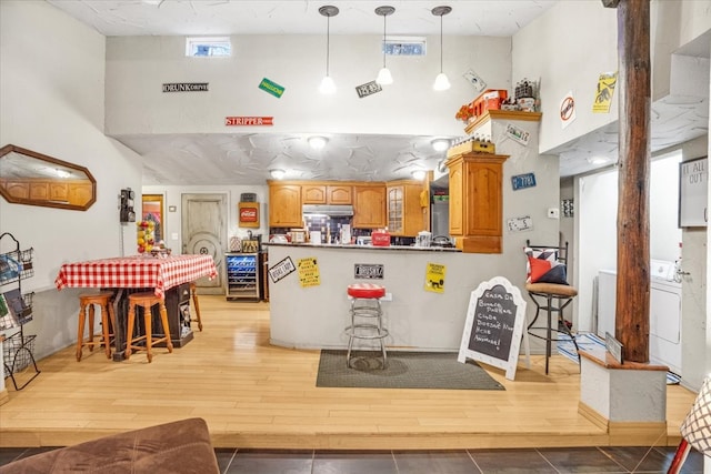 kitchen with pendant lighting, a high ceiling, light hardwood / wood-style floors, a kitchen bar, and washer / dryer