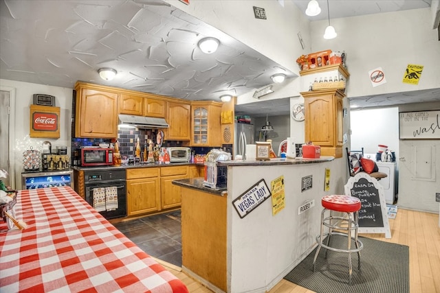 kitchen featuring kitchen peninsula, backsplash, black appliances, decorative light fixtures, and dark hardwood / wood-style floors