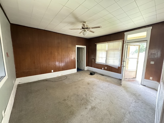 spare room featuring light carpet, ceiling fan, and wooden walls