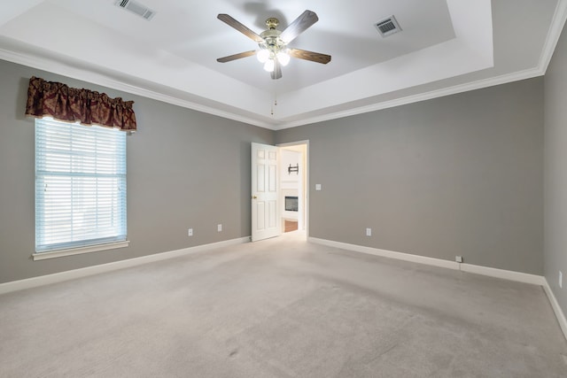 empty room with light carpet, a tray ceiling, ceiling fan, and crown molding