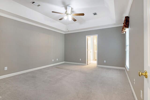 empty room featuring a raised ceiling, ceiling fan, crown molding, and light carpet