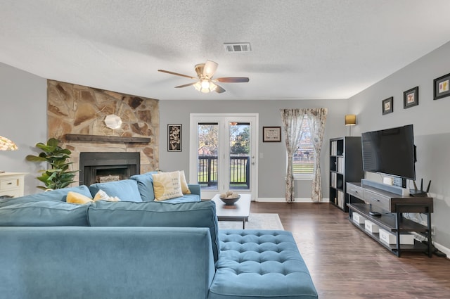 living room with a textured ceiling, a stone fireplace, ceiling fan, and dark wood-type flooring