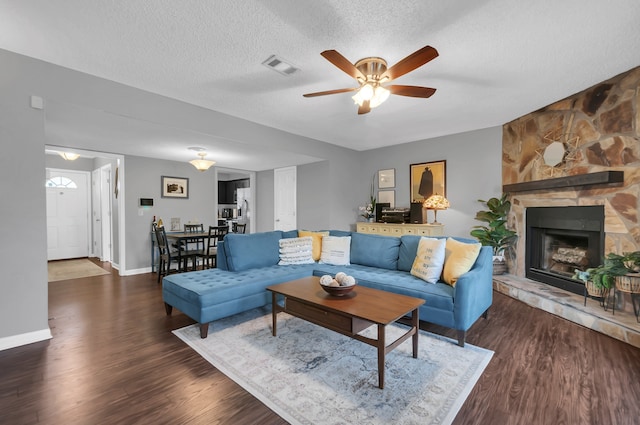 living room featuring dark hardwood / wood-style floors, ceiling fan, a stone fireplace, and a textured ceiling