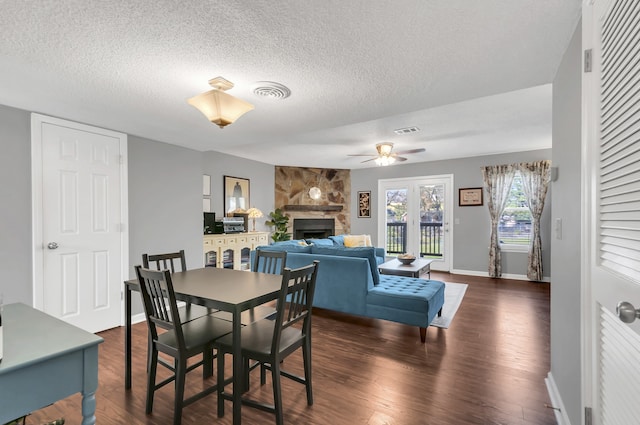 dining space with ceiling fan, a stone fireplace, dark hardwood / wood-style flooring, and a textured ceiling