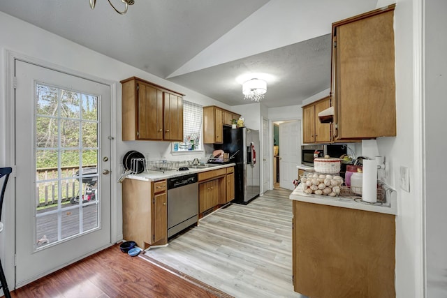 kitchen with a chandelier, lofted ceiling, appliances with stainless steel finishes, and light hardwood / wood-style flooring