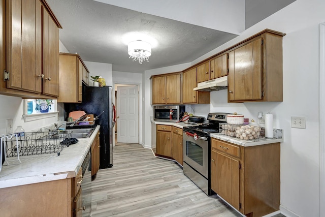 kitchen featuring sink, light wood-type flooring, a textured ceiling, and appliances with stainless steel finishes