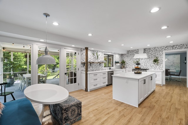 kitchen with light wood-type flooring, stainless steel dishwasher, sink, white cabinets, and hanging light fixtures