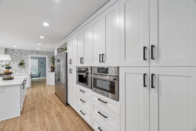 kitchen featuring backsplash, white cabinetry, stainless steel appliances, and light hardwood / wood-style flooring