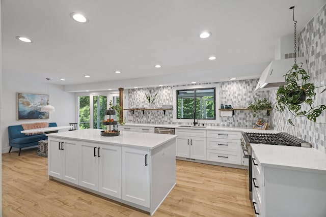 kitchen with stainless steel appliances, white cabinets, light hardwood / wood-style floors, decorative light fixtures, and a kitchen island