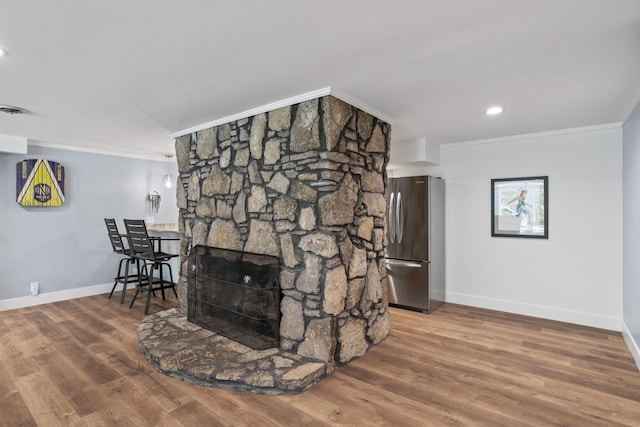 interior space with stainless steel refrigerator, hardwood / wood-style floors, a stone fireplace, and ornamental molding