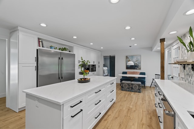 kitchen featuring white cabinetry, a center island, stainless steel appliances, light stone counters, and light hardwood / wood-style flooring