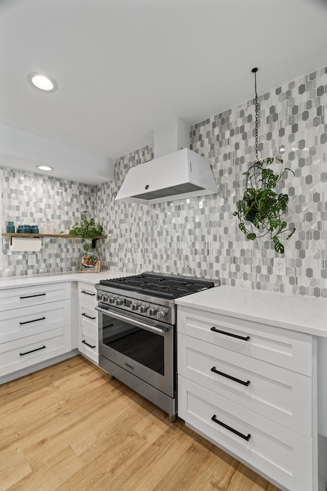 kitchen with premium range hood, stainless steel stove, decorative backsplash, light hardwood / wood-style floors, and white cabinetry