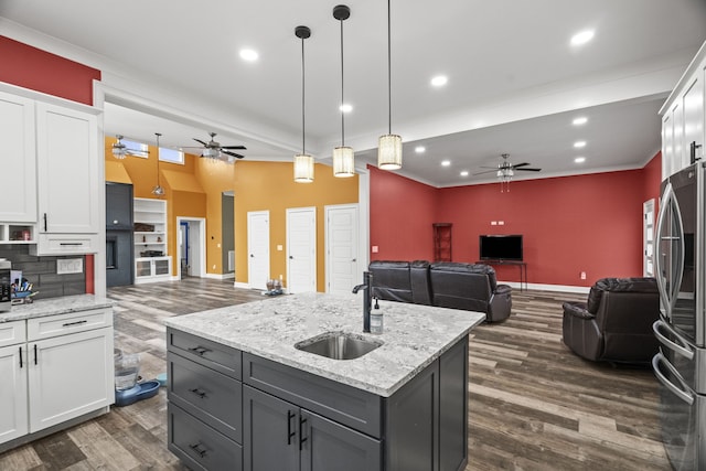 kitchen with sink, white cabinets, pendant lighting, stainless steel fridge, and a kitchen island with sink