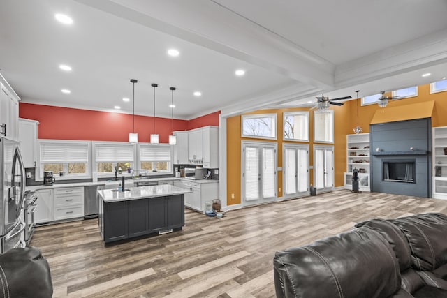 kitchen with white cabinets, hanging light fixtures, a kitchen island with sink, and beamed ceiling