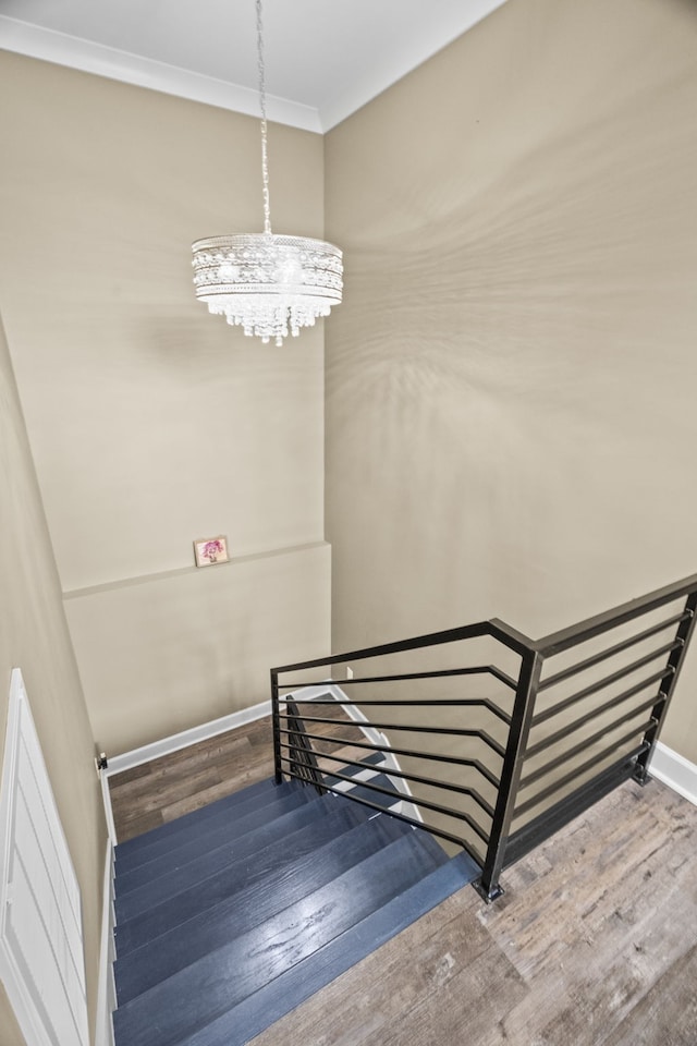 stairs with an inviting chandelier, hardwood / wood-style floors, and crown molding