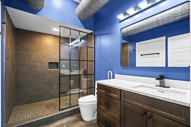 bathroom featuring toilet, a tile shower, vanity, and hardwood / wood-style flooring