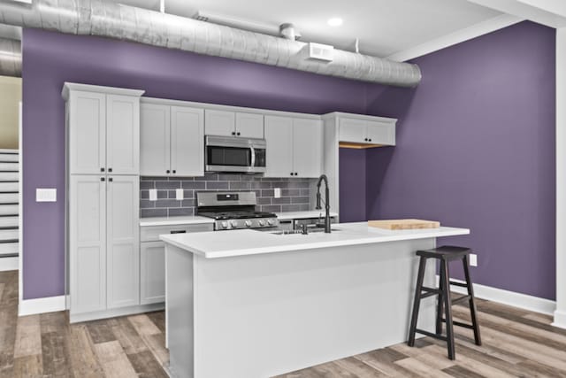 kitchen with stainless steel appliances, a center island with sink, and white cabinets