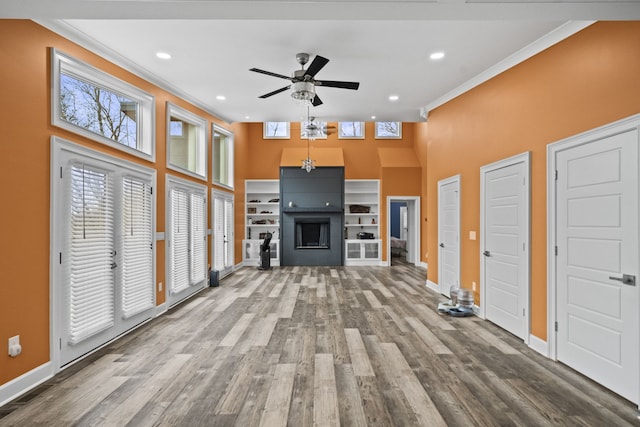 unfurnished living room with a high ceiling, ceiling fan, hardwood / wood-style floors, and ornamental molding